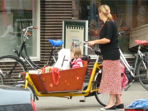 In the Netherlands, a mother cycles to the shops with her young daughter in the large container at the front of the bike.