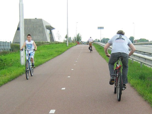 A boy rides down a hill on a wide cycle path in the Netherlands, safely protected from the busy road.