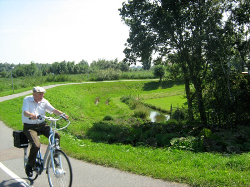 An elderly man rides his bike on a safe, wide, rural cycle path in the Netherlands