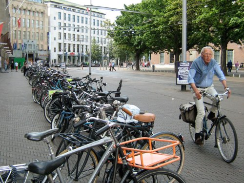 An older man rides his bike past hundreds of parked bikes in a city centre in the Netherlands
