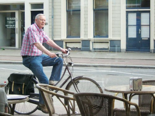 A late-middle-aged man calmly rides his bike past a cafe in the Netherlands