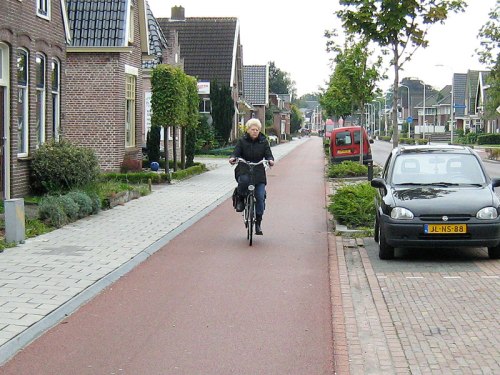 An older woman rides her bike along a cycle path, past houses with driveways