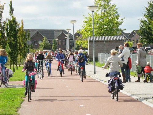 A photo of the school run at a school in the Netherlands. A wide cycle path is filled with children riding bikes.