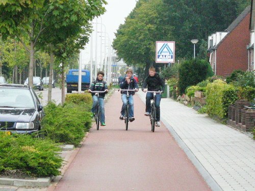 Three boys ride on a Dutch cyclepath, protected from the traffic on the road.
