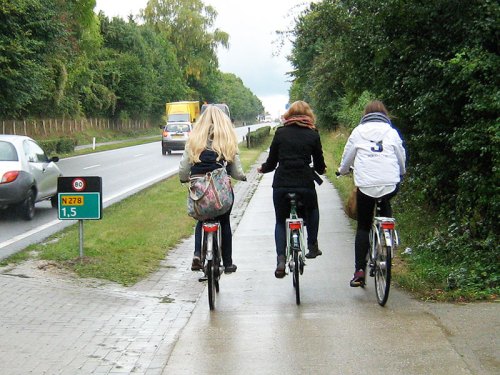 Three teenagers ride bikes on a rural cycle path in the Netherlands – up-hill!