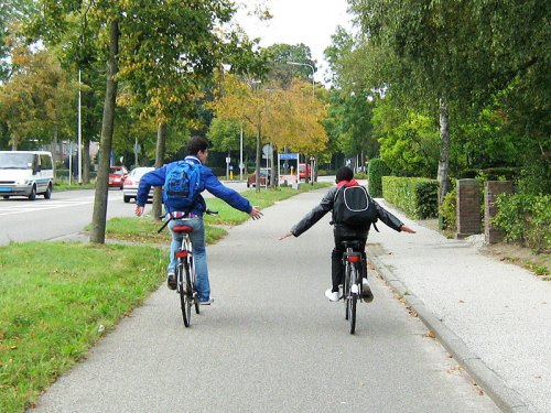 Two boys riding home from school, practising riding no-handed! They are safely on a cycle track away from the motor traffic.