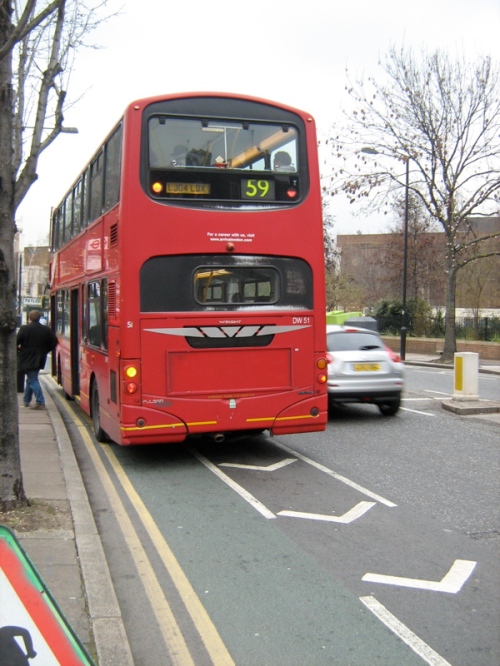 A photo of a bus from behind. The bus is stopped on the road, blocking the cycle lane but keeping the motor traffic flowing.