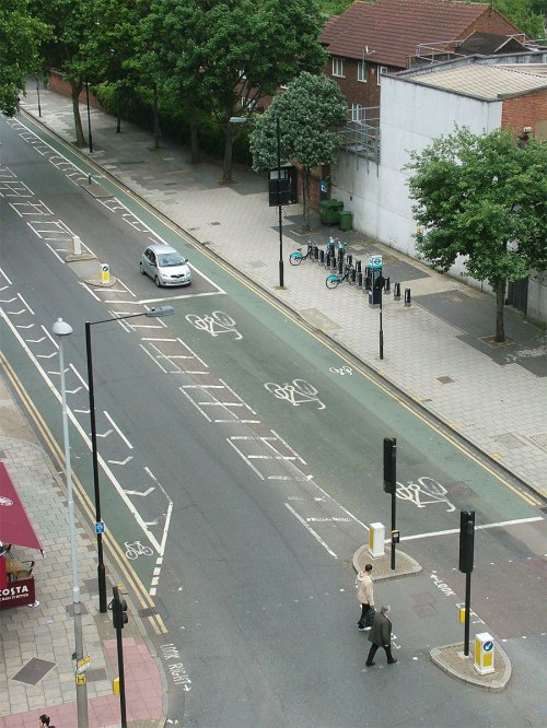 An altered photograph showing a junction with an extremely long (20m or so) ASZ, to demonstrate why ASLs aren't compatible with large numbers of people cycling.