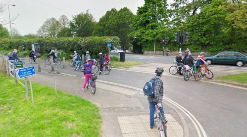 A photo of a cycle path next to a busy road near Cherwell School in Oxford. Many children on bikes are using the cycle path. None are using the main road.