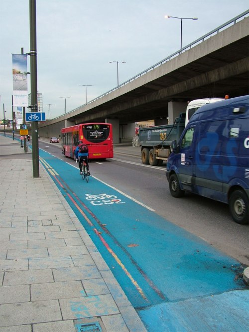 The footpath-level cycle path turns into a painted cycle lane. Note the HGV tyre marks have covered the blue within a day or two of it being painted.