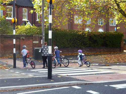 Photograph of a mother and three children walking with bikes on a zebra crossing.