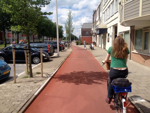 A young woman rides on a wide red-asphalt cycleway in Utrecht. There is room for four people to cycle side-by-side.